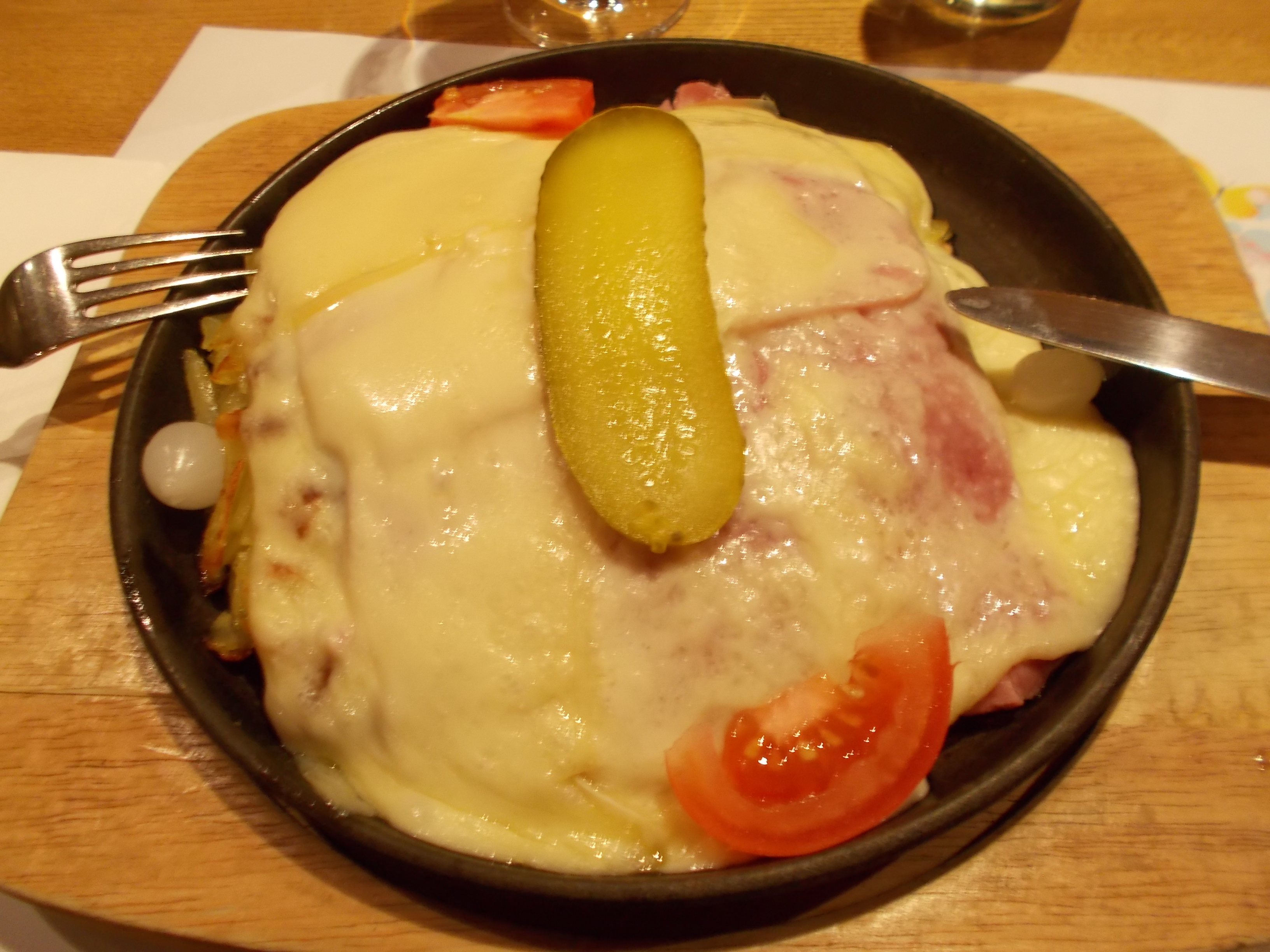 A cast iron plate filled with rösti, cheese, fresh tomato, and a pickle.