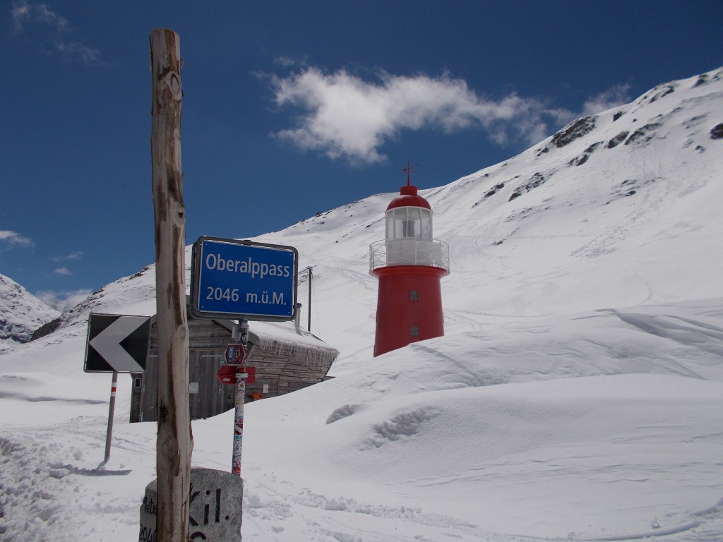 A red and white lighthouse partly buried in snow on the flanks of a Swiss mountain.