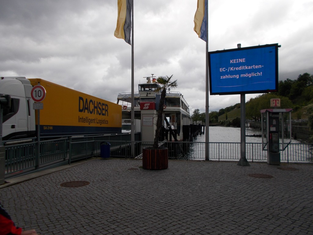 A large truck driving off a ferry with the lake in the background.