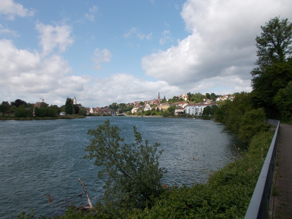 The town of Laufenburg in Germany and Switzerland viewed from a distance with the Rhine river in the foreground. Cloudy skies above.