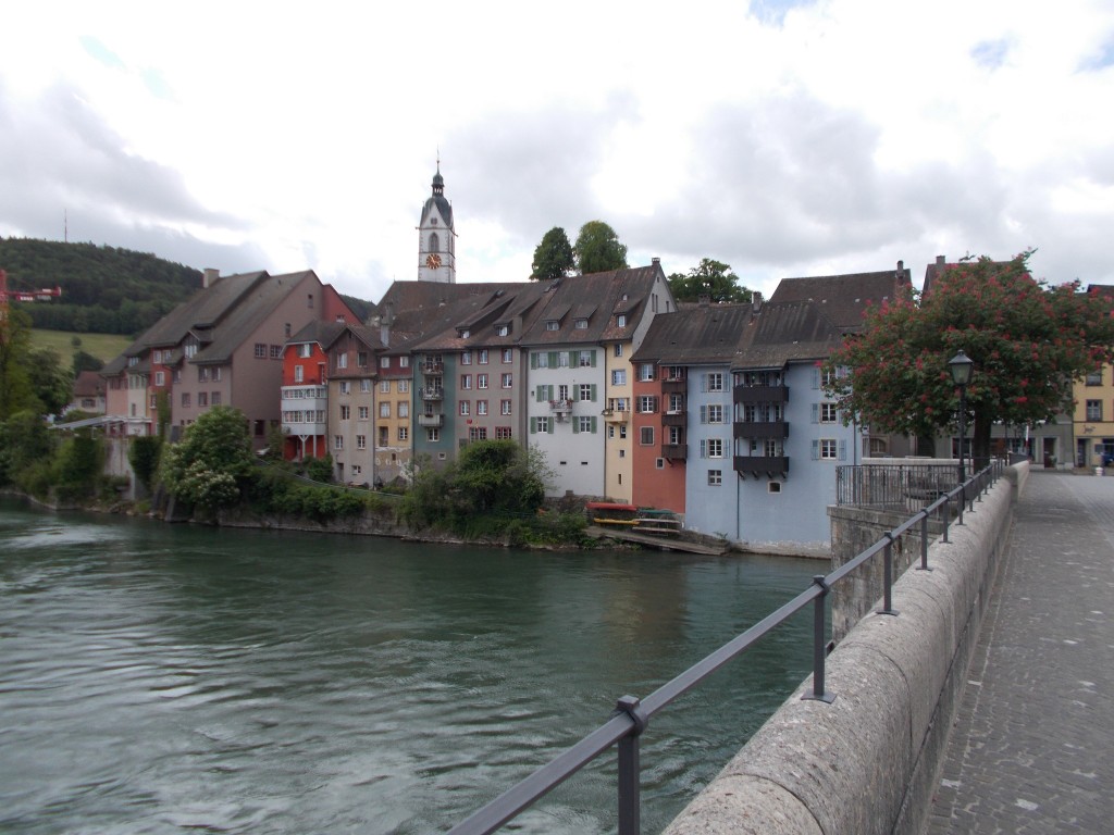 A row of colourful buildings at the edge of the Rhine river photographed from a bridge.