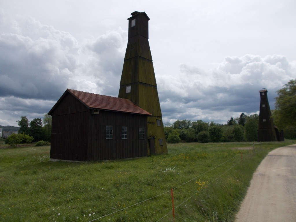 Two green wooden towers standing in a field with a gravel road to the right.