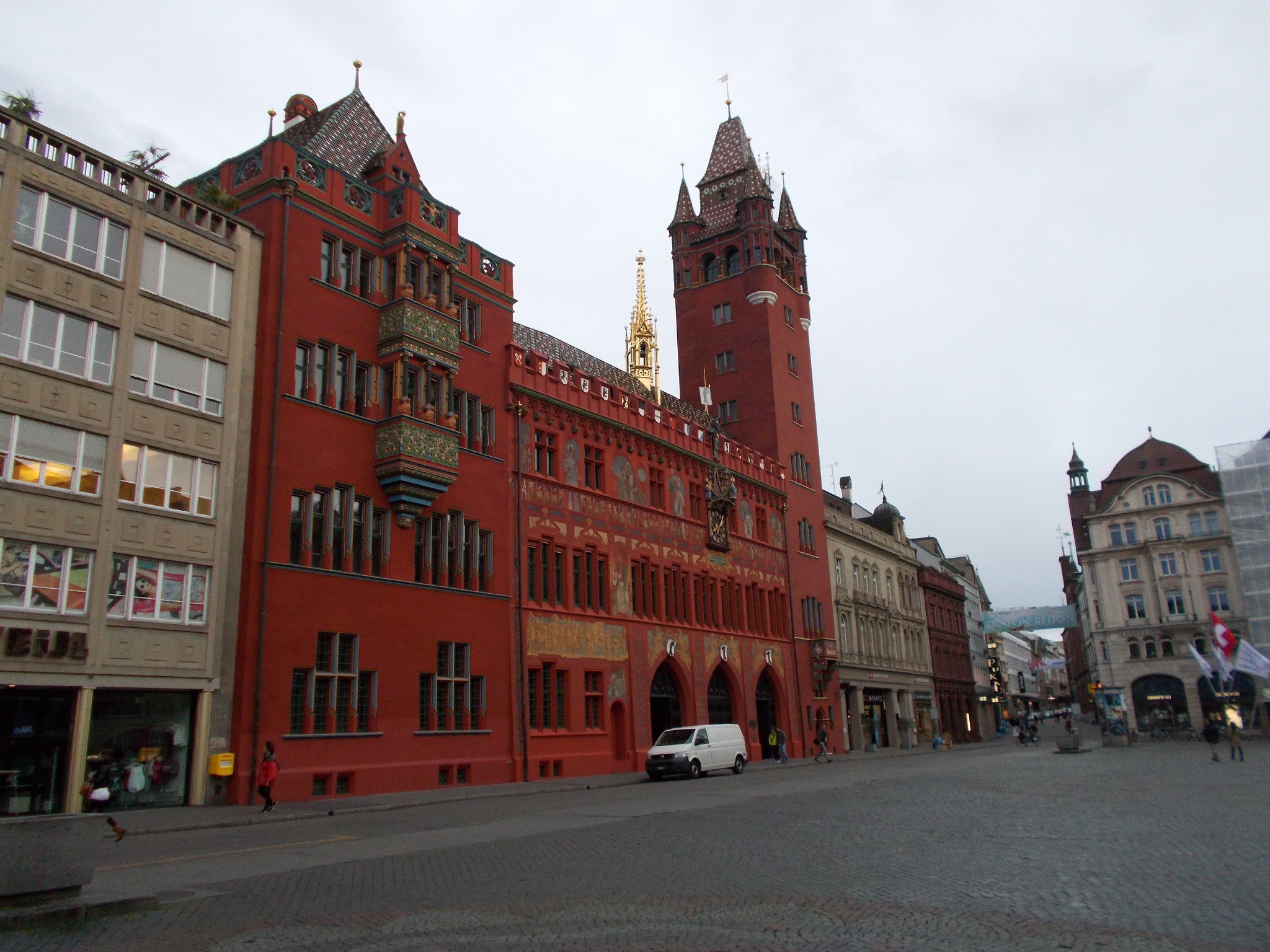 A bright red ornate building on the edge of a large city market square.