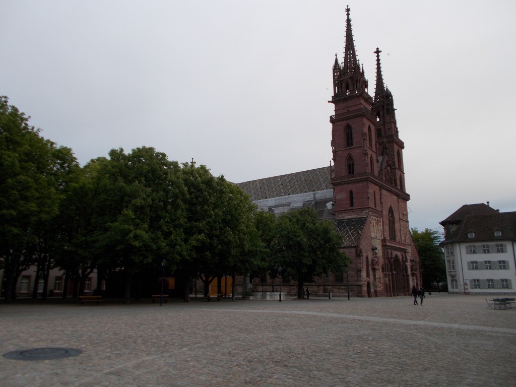 A huge cathedral sitting in a town square with large trees in the foreground.